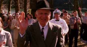 Movie still from “Big Fish” (2003), directed by Tim Burton – An older man in a suit and hat waves to the crowd; Medium shot, Over the shoulder angle