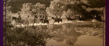 Movie still from “Big Jake” (1971), directed by George Sherman – A group of people riding horses across a body of water; Wide shot, High angle