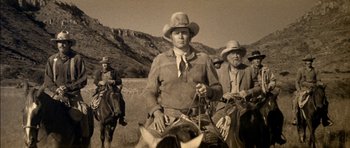 Movie still from “Big Jake” (1971), directed by George Sherman – Two men on horses in a field with mountains in the background; Medium shot, Low angle