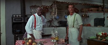 Movie still from “Big Jake” (1971), directed by George Sherman – A couple of men standing next to each other in front of a table; Medium shot, Low angle