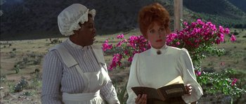 Movie still from “Big Jake” (1971), directed by George Sherman – Two women standing next to each other holding a book; Medium shot, Over the shoulder angle