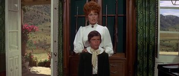 Movie still from “Big Jake” (1971), directed by George Sherman – A woman and a young boy standing next to each other; Medium shot, Low angle