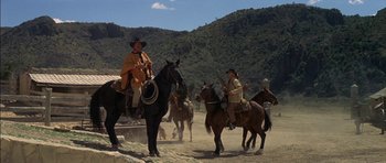 Movie still from “Big Jake” (1971), directed by George Sherman – A group of men riding horses across a dirt field; Wide shot, Low angle