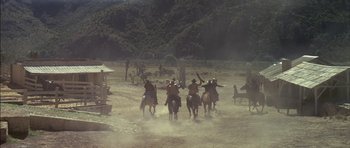 Movie still from “Big Jake” (1971), directed by George Sherman – A group of people riding horses on a dirt field; Extreme Wide shot, Low angle