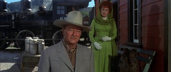 Movie still from “Big Jake” (1971), directed by George Sherman – A man and a woman standing next to each other in front of a train; Medium shot, Over the shoulder angle