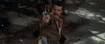 Movie still from “Big Jake” (1971), directed by George Sherman – A man holding a gun while kneeling on the ground; Close Up shot, Low angle