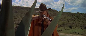 Movie still from “Big Jake” (1971), directed by George Sherman – A man in a cowboy hat is holding a gun; Medium shot, Low angle