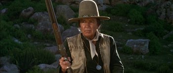 Movie still from “Big Jake” (1971), directed by George Sherman – An older man holding a rifle in a hat; Close Up shot, Low angle