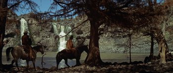 Movie still from “Big Jake” (1971), directed by George Sherman – A man riding a horse next to a waterfall; Extreme Wide shot, Low angle