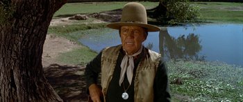 Movie still from “Big Jake” (1971), directed by George Sherman – An older man wearing a cowboy hat and vest; Medium shot, Over the shoulder angle