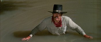 Movie still from “Big Jake” (1971), directed by George Sherman – A man wearing a cowboy hat is in a body of water; Medium shot, High angle