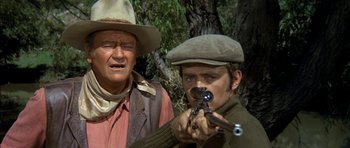 Movie still from “Big Jake” (1971), directed by George Sherman – A man holding a gun while standing next to another man; Close Up shot, Over the shoulder angle