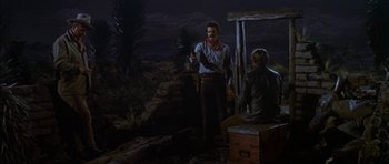 Movie still from “Big Jake” (1971), directed by George Sherman – Two men in cowboy garb standing next to an old trunk; Wide shot, Over the shoulder angle
