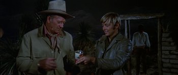 Movie still from “Big Jake” (1971), directed by George Sherman – A man and a woman are holding a drink; Medium shot, Over the shoulder angle