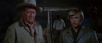 Movie still from “Big Jake” (1971), directed by George Sherman – A man standing next to another man in a cave; Medium shot, Over the shoulder angle