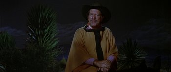 Movie still from “Big Jake” (1971), directed by George Sherman – An older man wearing a cowboy hat and poncho; Medium shot, Low angle