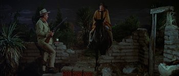 Movie still from “Big Jake” (1971), directed by George Sherman – A man riding a horse in a cave with a gun in his hand; Wide shot, Low angle