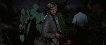 Movie still from “Big Jake” (1971), directed by George Sherman – A man holding a gun while standing next to a cactus; Medium shot, Low angle