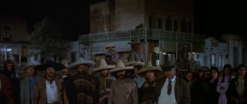 Movie still from “Big Jake” (1971), directed by George Sherman – A group of men wearing sombreros standing next to each other in front of a building; Wide shot, Low angle