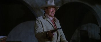 Movie still from “Big Jake” (1971), directed by George Sherman – An older man holding a gun while wearing a hat; Medium shot, Low angle