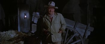 Movie still from “Big Jake” (1971), directed by George Sherman – A man in a hat holding a gun in his hand; Medium shot, Over the shoulder angle
