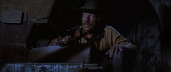 Movie still from “Big Jake” (1971), directed by George Sherman – A man in a cowboy hat holding a knife; Medium shot, Low angle