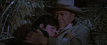 Movie still from “Big Jake” (1971), directed by George Sherman – An older man holding a young boy in his arms; Medium shot, High angle