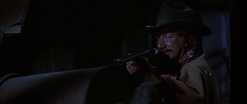 Movie still from “Big Jake” (1971), directed by George Sherman – A man in a cowboy hat smoking a pipe; Close Up shot, Over the shoulder angle