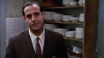 Movie still from “Big Night” (1996), directed by Stanley Tucci – A man wearing a suit and tie in front of stacks of plates; Close Up shot, Over the shoulder angle