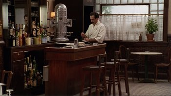 Movie still from “Big Night” (1996), directed by Stanley Tucci – A man sitting at a bar in front of a microphone; Wide shot, High angle