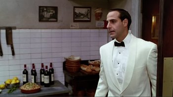 Movie still from “Big Night” (1996), directed by Stanley Tucci – A man in a white tuxedo standing in a kitchen next to bottles of wine; Medium shot, Over the shoulder angle