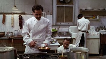Movie still from “Big Night” (1996), directed by Stanley Tucci – A man standing in front of a stove holding a pan; Medium shot, Low angle