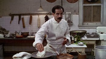 Movie still from “Big Night” (1996), directed by Stanley Tucci – A man in a white chef's outfit in a kitchen preparing food; Medium shot, Low angle