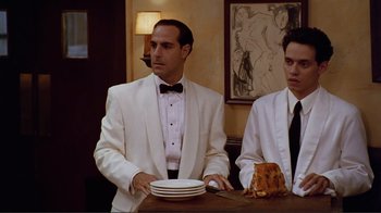 Movie still from “Big Night” (1996), directed by Stanley Tucci – A man in a white suit and tie standing at a table with plates; Medium shot, Low angle