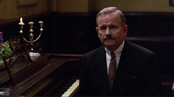 Movie still from “Big Night” (1996), directed by Stanley Tucci – An older man wearing a suit and tie standing in front of a piano; Close Up shot, Low angle