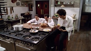 Movie still from “Big Night” (1996), directed by Stanley Tucci – A group of men sitting at a table in a kitchen; Wide shot, High angle