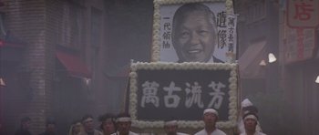 Movie still from “Big Trouble in Little China” (1986), directed by John Carpenter – A group of men standing in front of a portrait; Medium shot, Low angle