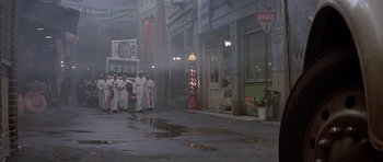 Movie still from “Big Trouble in Little China” (1986), directed by John Carpenter – A group of men in white robes walking down a street; Extreme Wide shot, High angle