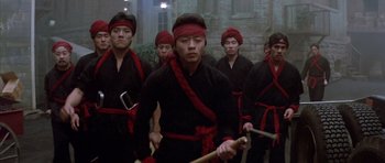 Movie still from “Big Trouble in Little China” (1986), directed by John Carpenter – A group of men in black shirts and red bandannas; Medium shot, Low angle