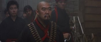 Movie still from “Big Trouble in Little China” (1986), directed by John Carpenter – A man with a beard is wearing a black shirt and red bandanna; Close Up shot, Low angle