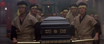 Movie still from “Big Trouble in Little China” (1986), directed by John Carpenter – A group of men standing next to a black coffin; Wide shot, Low angle
