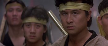 Movie still from “Big Trouble in Little China” (1986), directed by John Carpenter – A man with a sword in his mouth and another man with a headband in front of him; Close Up shot, Low angle