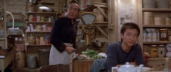 Movie still from “Big Trouble in Little China” (1986), directed by John Carpenter – A man standing in front of a table holding a large knife; Medium shot, Over the shoulder angle