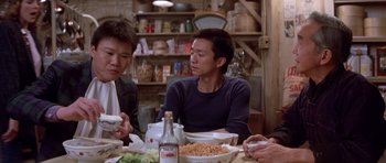 Movie still from “Big Trouble in Little China” (1986), directed by John Carpenter – A group of people sitting at a table eating food; Medium shot, Over the shoulder angle