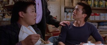 Movie still from “Big Trouble in Little China” (1986), directed by John Carpenter – Two people are sitting at a table and one of them is holding chopsticks; Medium shot, Over the shoulder angle