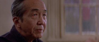 Movie still from “Big Trouble in Little China” (1986), directed by John Carpenter – An older man looking at the camera while sitting in a room; Close Up shot, Low angle