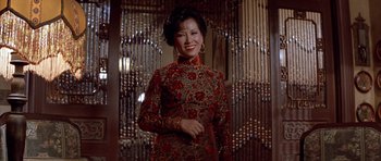 Movie still from “Big Trouble in Little China” (1986), directed by John Carpenter – A woman in a red and gold dress standing in front of a glass door; Medium shot, High angle