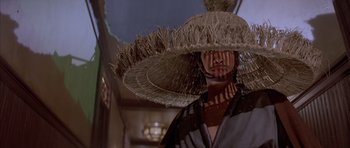 Movie still from “Big Trouble in Little China” (1986), directed by John Carpenter – A person wearing a straw hat and a black and white striped shirt; Close Up shot, Low angle