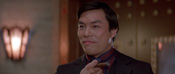 Movie still from “Big Trouble in Little China” (1986), directed by John Carpenter – A person wearing a suit holding a cigar; Close Up shot, Low angle