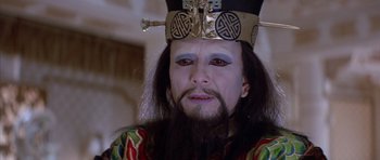 Movie still from “Big Trouble in Little China” (1986), directed by John Carpenter – A man with long black hair and a beard wearing a gold crown; Close Up shot, High angle